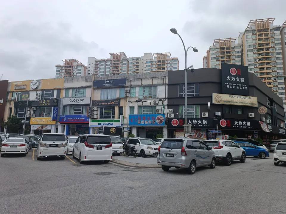 Deretan kedai dengan papan tanda restoran steamboat, kedai serbaneka dan klinik, kereta diletak di hadapan