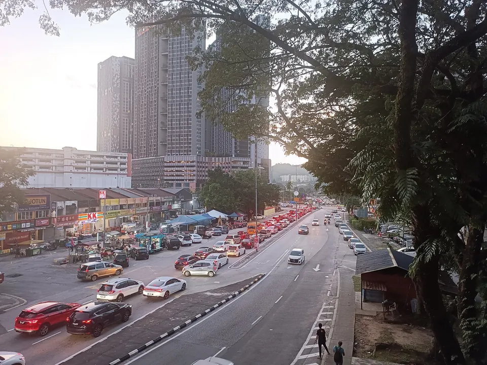 Jalan Kuchai Lama at dusk: roadside stalls in front of shoplots, evening traffic and tower blocks behind